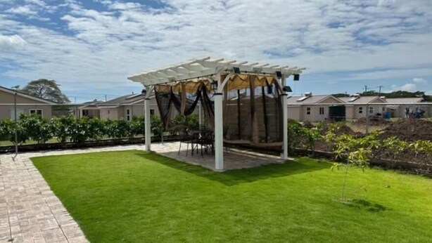 A covered outdoor seating area with a pergola structure, surrounded by a well-maintained lawn and a paved walkway.