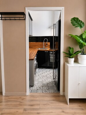 Una cocina con mostrador de madera, suelo con estampado blanco y negro, y una planta en maceta sobre un mueble.