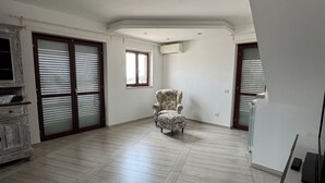 A spacious room with a herringbone-patterned wooden floor, a floral armchair, and a built-in wardrobe with a mirror. - PIRGUS ATTIC (Santa Marinella)