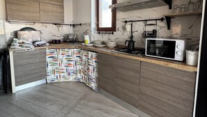 A modern kitchen with wooden cabinets, a microwave, and a window. - PIRGUS ATTIC (Santa Marinella)