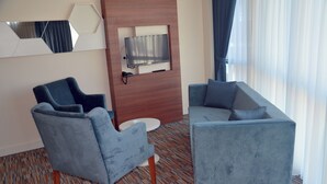 Quarto de hotel moderno com sofá, poltrona e televisão de tela plana fixada em um painel de madeira.