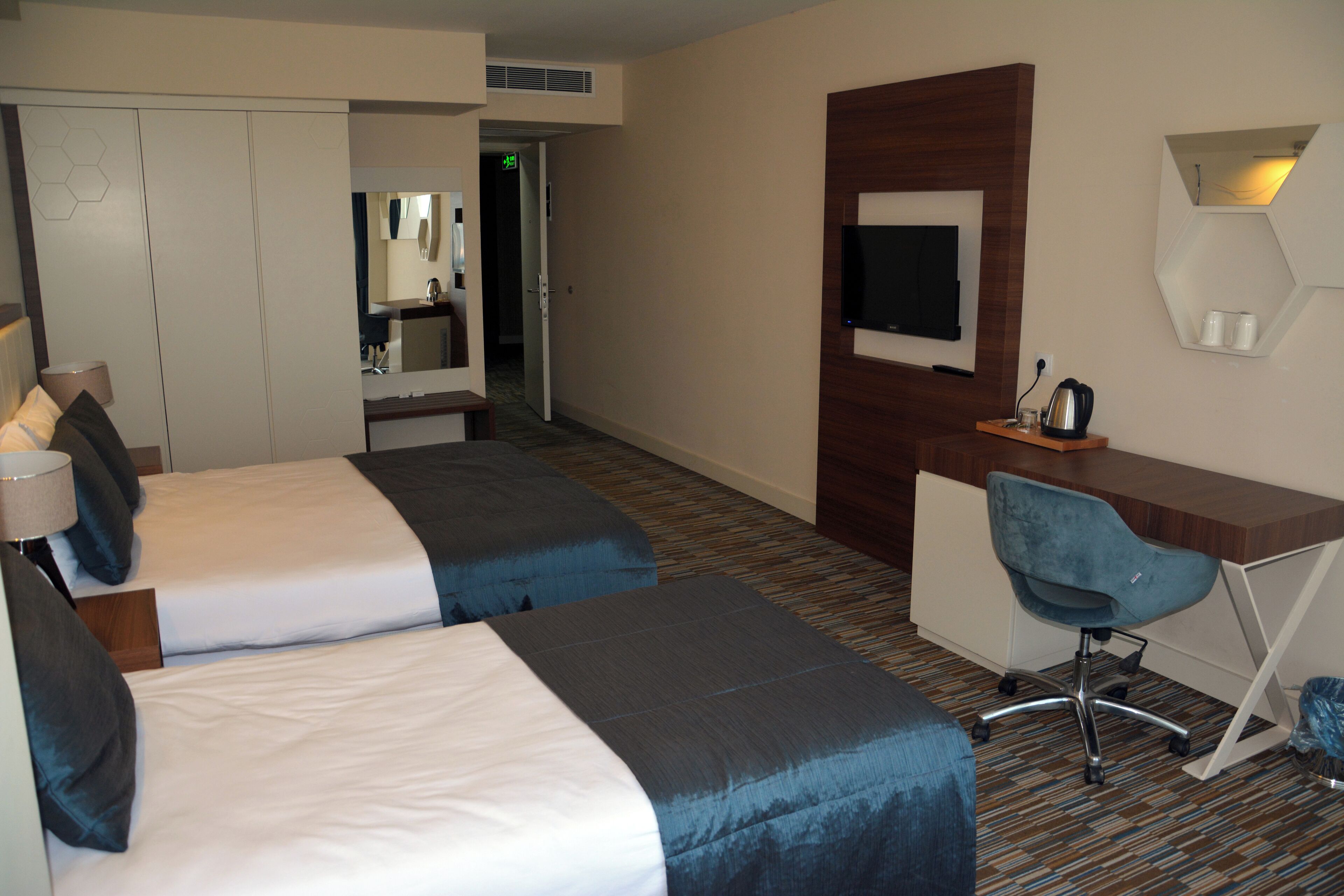 Habitación de hotel con dos camas, un escritorio, una silla, un televisor y un espejo.