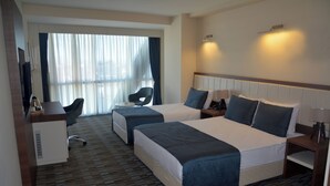 Quarto de hotel com duas camas, uma mesa, uma cadeira e uma televisão.