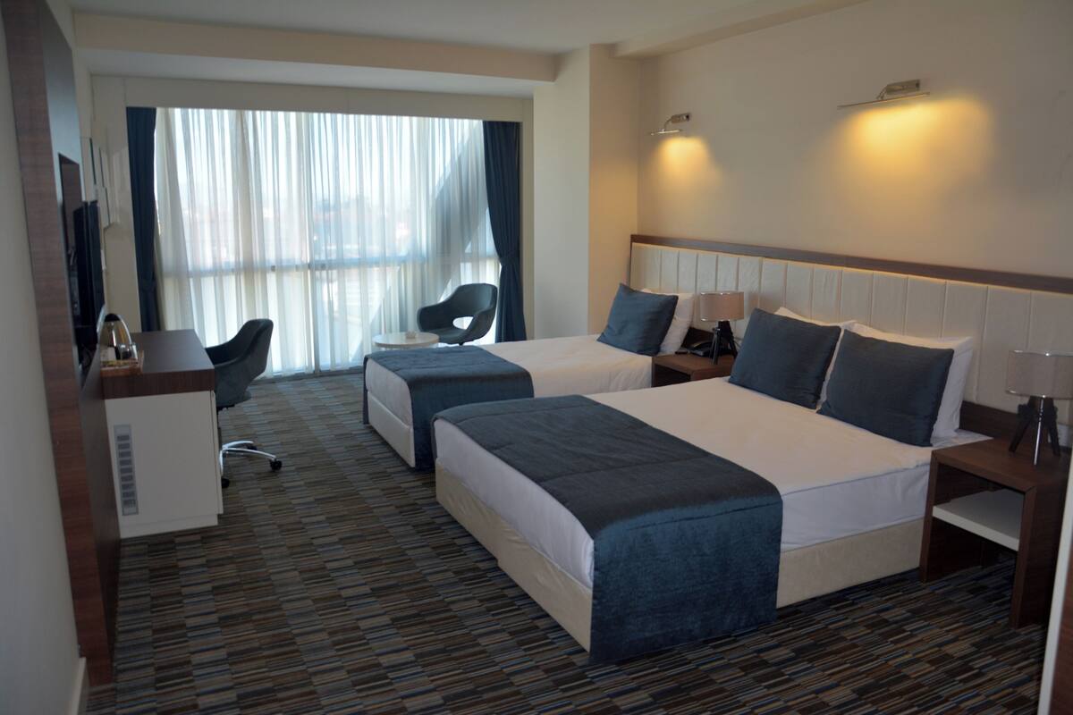 Ein Hotelzimmer mit zwei Betten, einem Schreibtisch, einem Sessel und einem Fernseher.