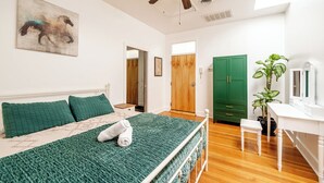 Une chambre à coucher avec un lit, un ventilateur de plafond, une porte verte et une plante en pot.