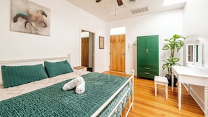 Ein Schlafzimmer mit Bett, Deckenventilator, grüner Tür und Zimmerpflanze.