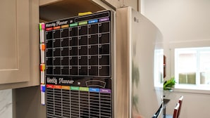 Una cocina con refrigerador y un planificador mensual y semanal colgado en la pared.