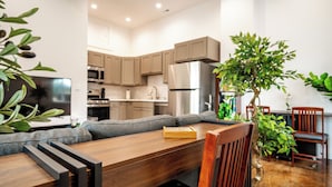 Una cocina moderna con electrodomésticos integrados, un comedor con mesa y sillas de madera, y una planta verde grande.