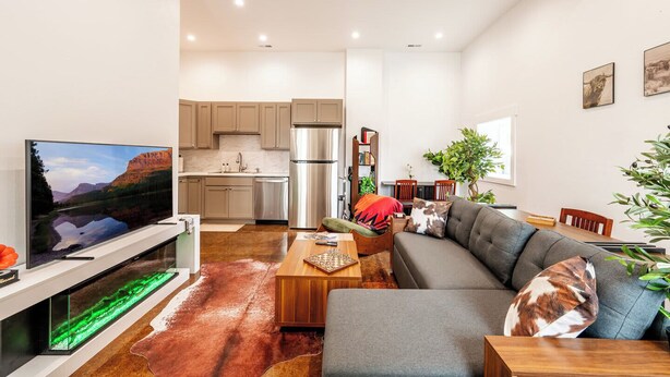 Una sala de estar moderna con una televisión de pantalla plana, un sofá, una mesa de centro de madera y una zona de cocina con armarios y un refrigerador.