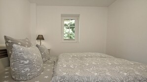 A bedroom with a bed, pillows, a nightstand, a lamp, and a window. - Modernes Appartement mit Balkon, Wiek (Wiek)