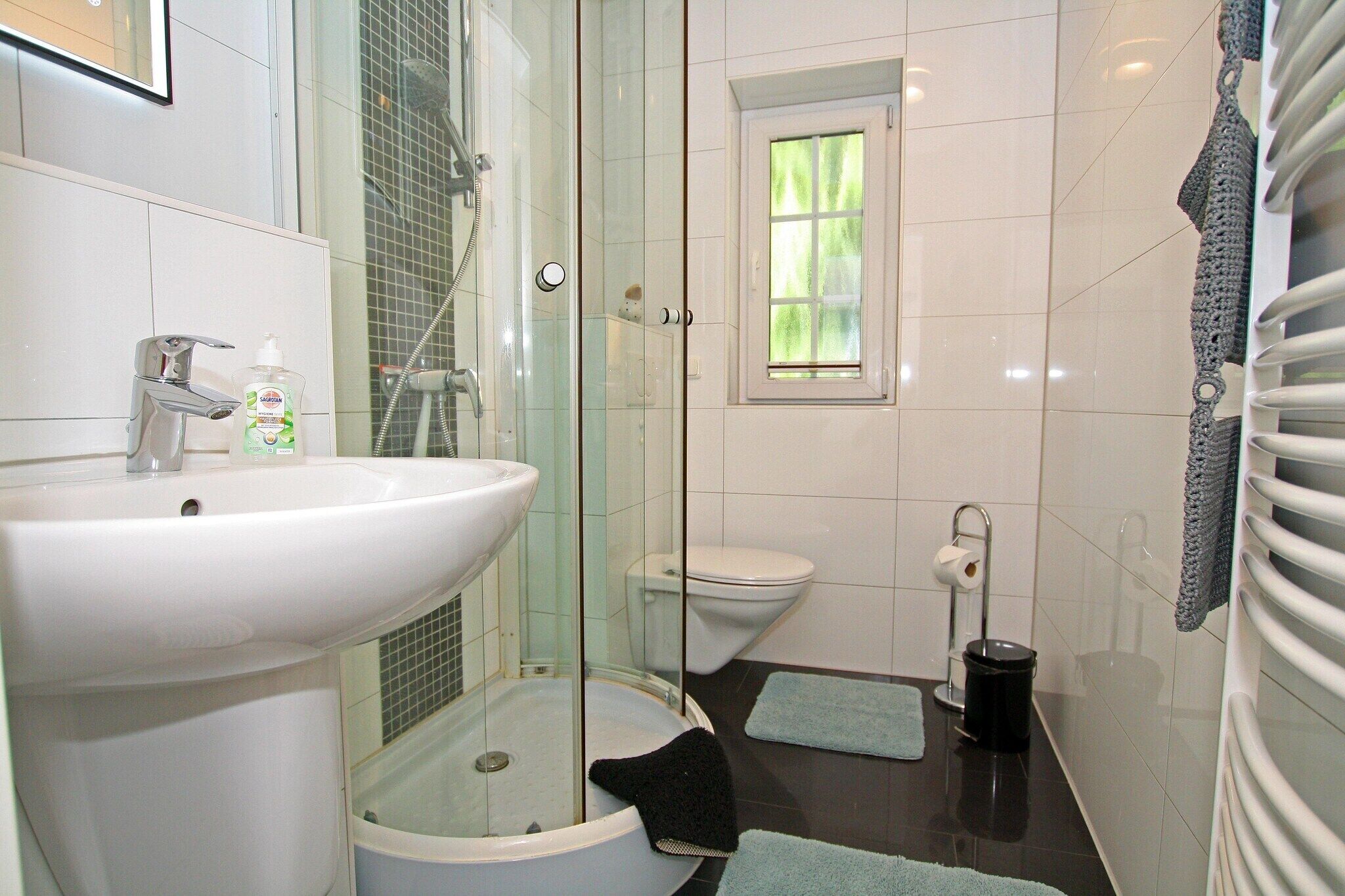 Un baño con ducha acristalada, un lavabo blanco, un inodoro y una ventana pequeña.