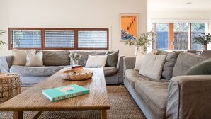 A living room with a sofa set, a coffee table with a book, and a window with blinds.