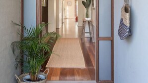 A hallway with a sliding glass door leading to a room, a potted plant, a woven bag, and a wooden floor.