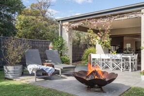 Un patio trasero con una fogata, asientos al aire libre y una pérgola.