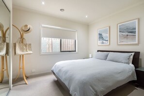 Un dormitorio con cama, una ventana con persianas, una mesita de noche y dos cuadros enmarcados en la pared.