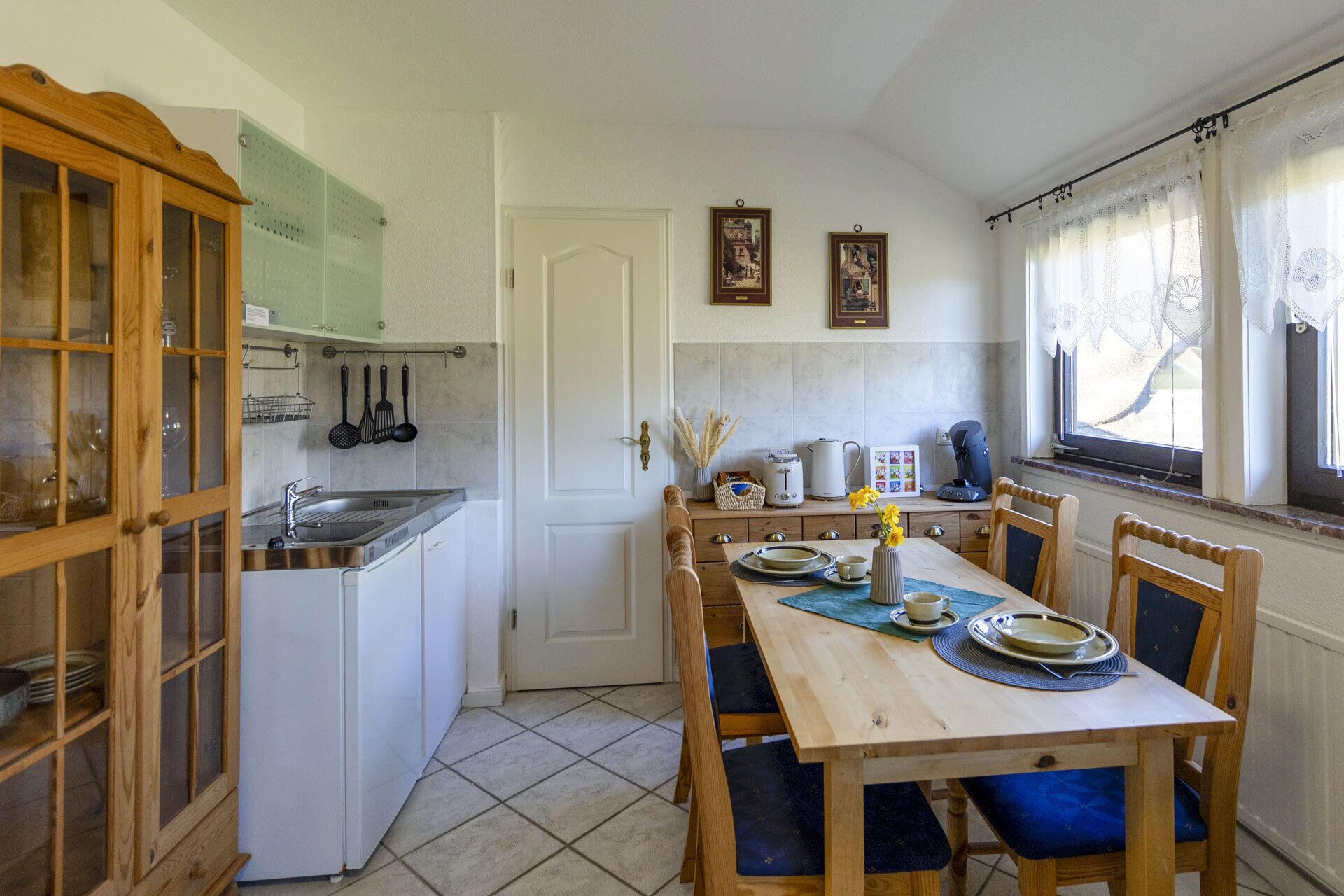 A compact kitchen with a dining area, featuring a wooden table, chairs, and a cabinet with glass doors.