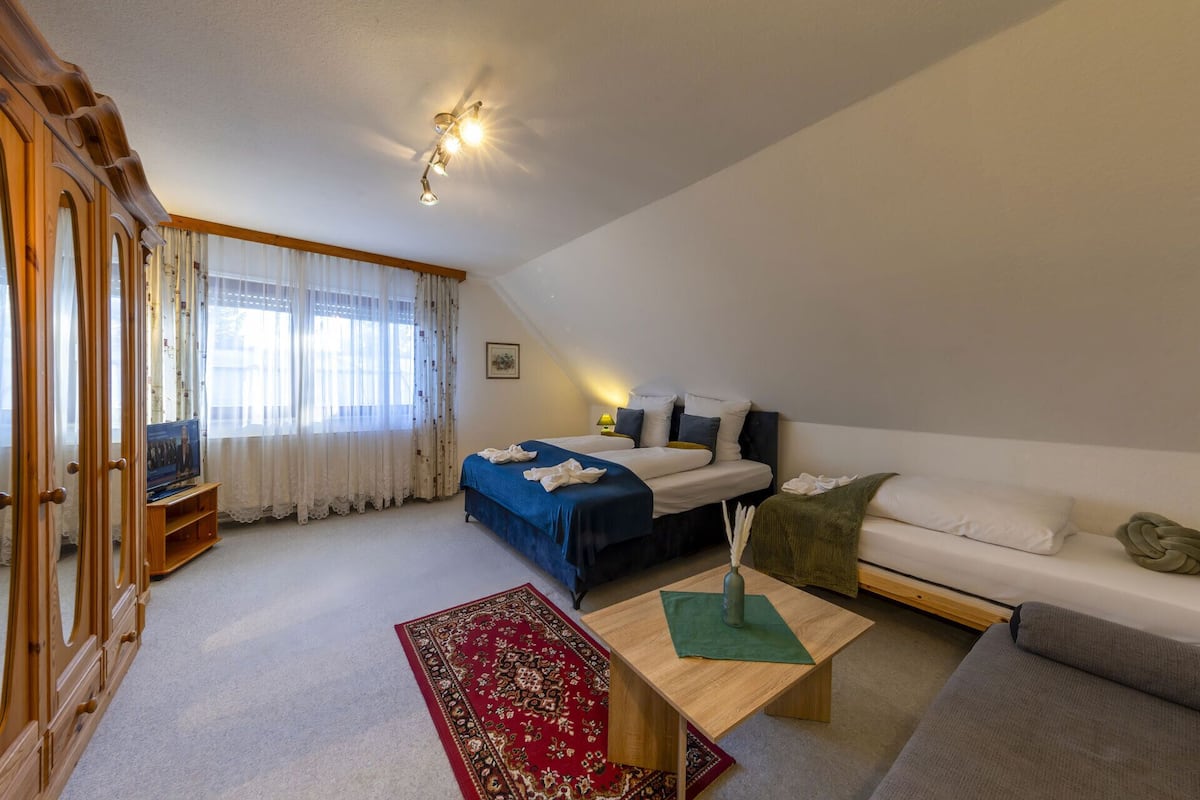 A bedroom with a bed, a sofa, a small table, and a window with curtains.