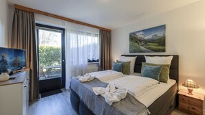 A bedroom with a bed, a bedside table, a lamp, a painting, and a window with curtains. - AMAYA Hotel & Suites (Soltau)