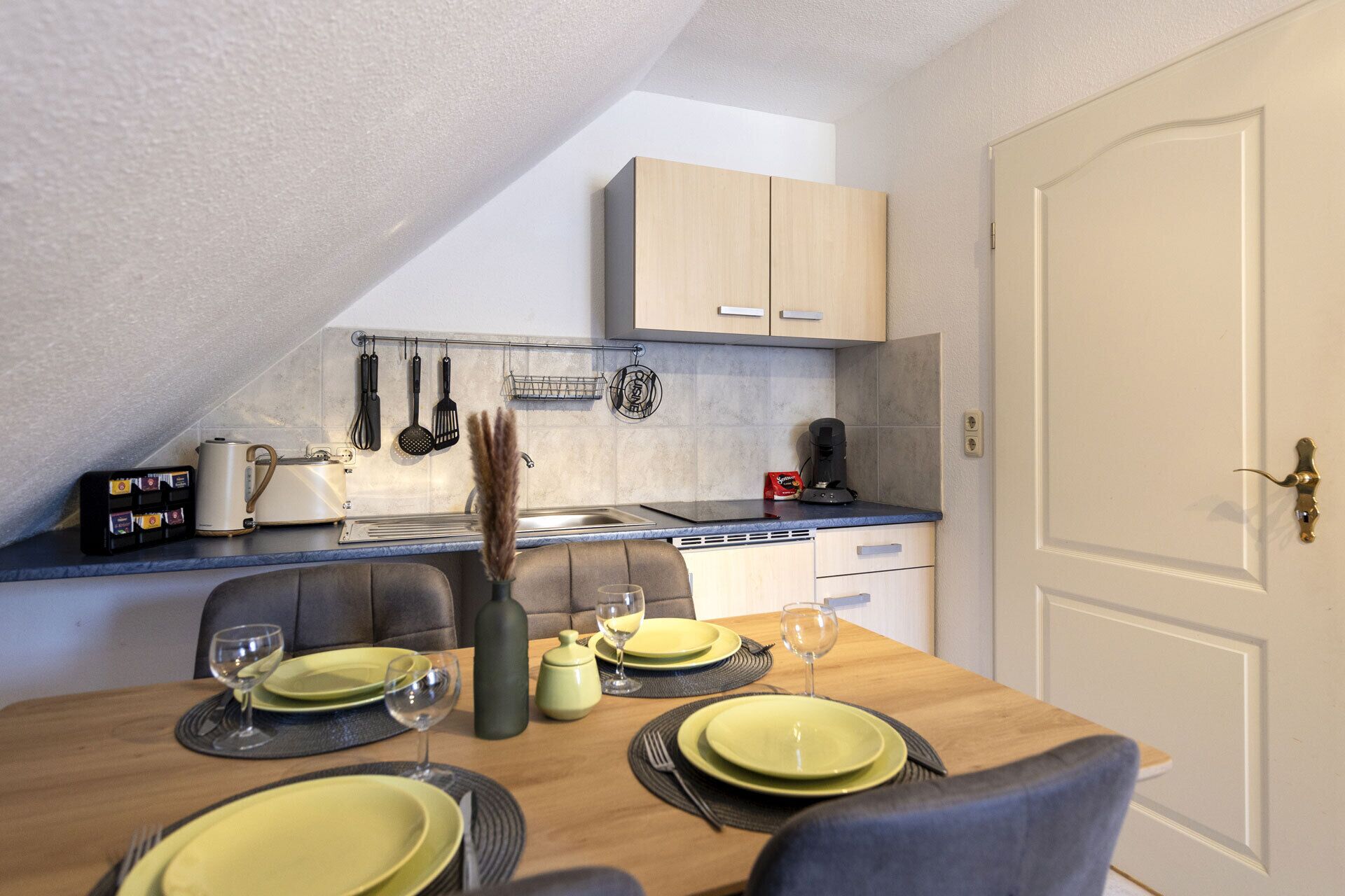 A compact kitchen with a dining table set for four, a coffee machine, and various kitchen utensils.