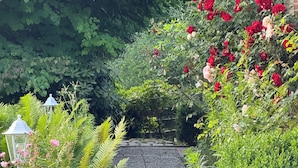 A garden pathway with a brick surface leading to a building with a thatched roof. - AMAYA Hotel & Suites (Soltau)