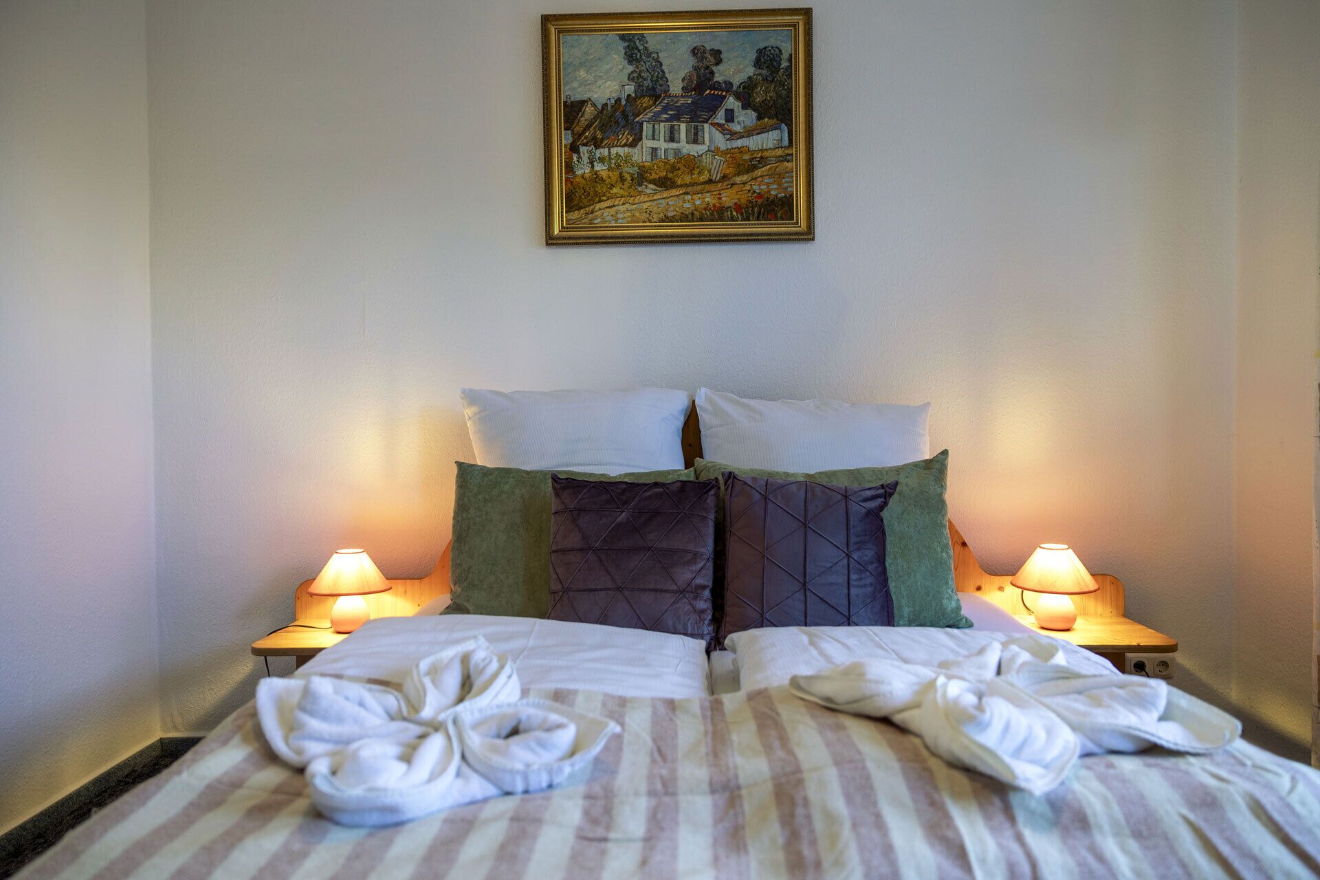 Une chambre d’hôtel avec un lit, deux oreillers, deux lampes de chevet et un tableau au mur.