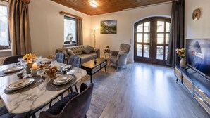 A living room with a dining area, a sofa, a TV, and a fireplace. - AMAYA Hotel & Suites (Soltau)