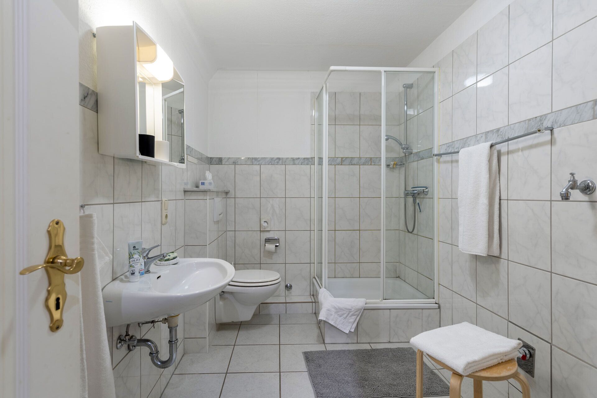 A modern bathroom with a glass shower enclosure, a sink, toilet, and a small stool with a towel.