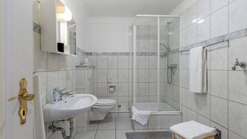 A modern bathroom with a glass shower enclosure, a sink, toilet, and a small stool with a towel.