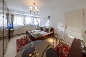 A bedroom with a bed, bedside table, lamp, and a television on a stand. - AMAYA Hotel & Suites (Soltau)
