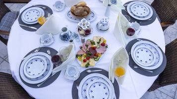 A round table set for breakfast with plates, cutlery, and a variety of food items including bread, pastries, and a charcuterie board.