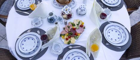 A round table set for breakfast with plates, cutlery, and a variety of food items including bread, pastries, and a charcuterie board.