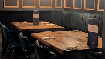 A restaurant with dark wooden tables and black leather booths, framed pictures on the walls, and a menu stand.
