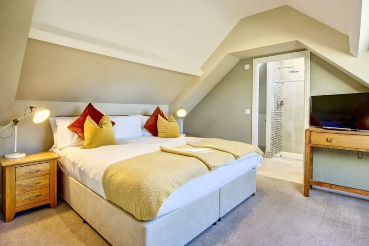 A bedroom with a bed, bedside tables, a TV, and a door leading to another room.