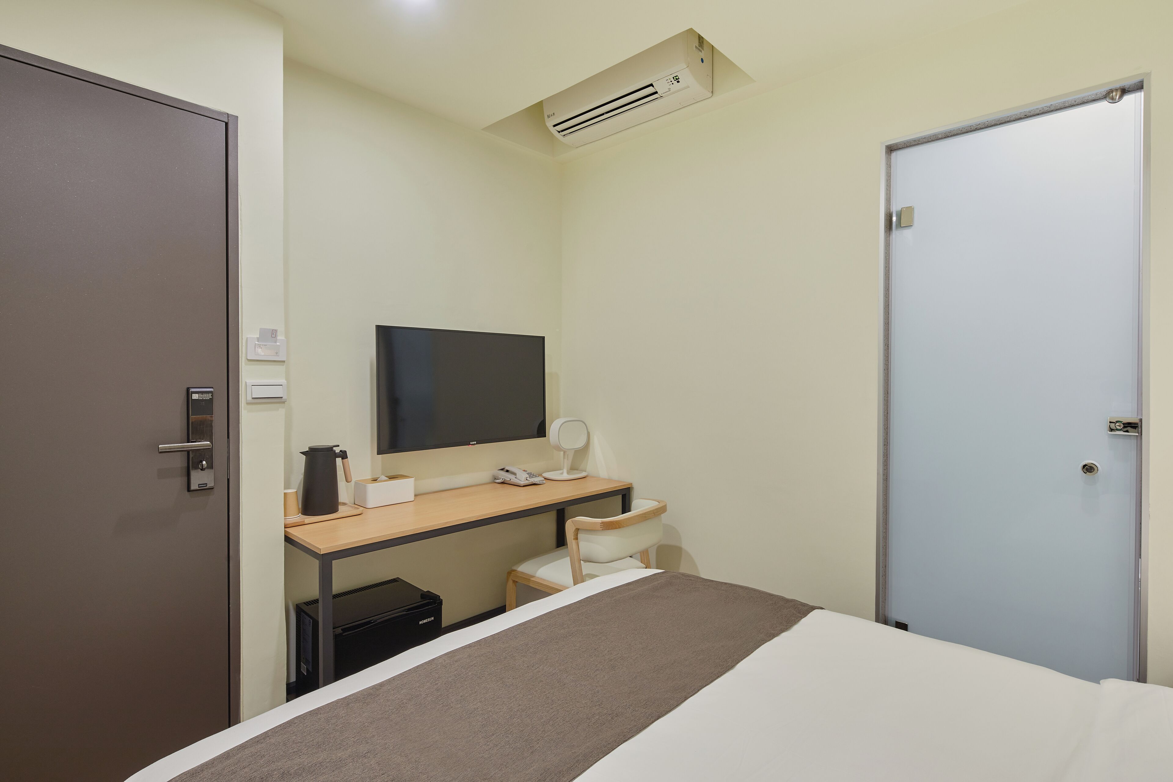 Una habitación de hotel con una cama, un escritorio con una computadora, una silla, un televisor y un aire acondicionado.