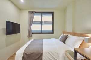 Une chambre d’hôtel avec un lit, un téléviseur fixé au mur, une fenêtre avec des rideaux et une table de chevet.