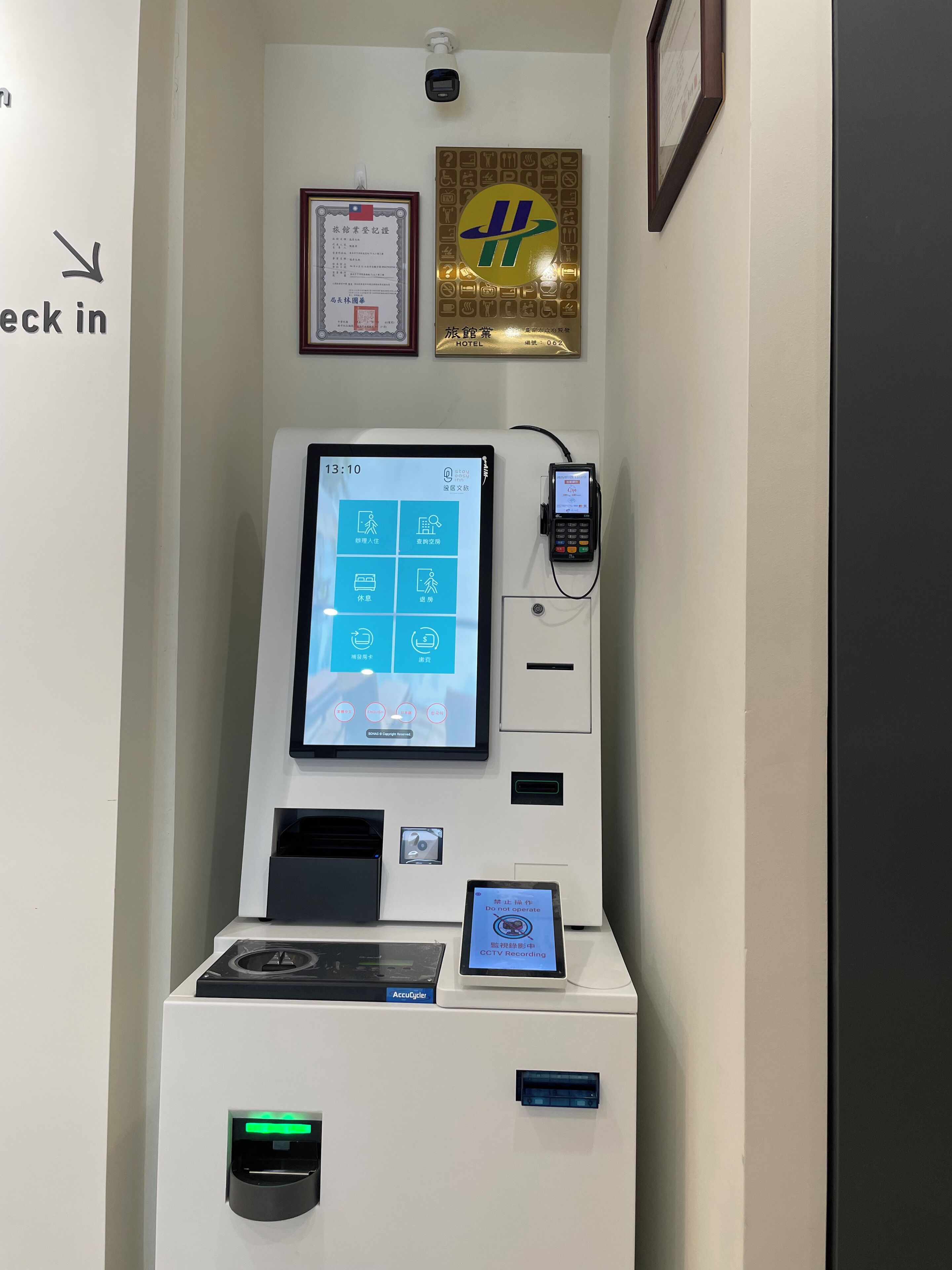 A self-service kiosk with a digital screen displaying various options, a card reader, and a CCTV recording sign.