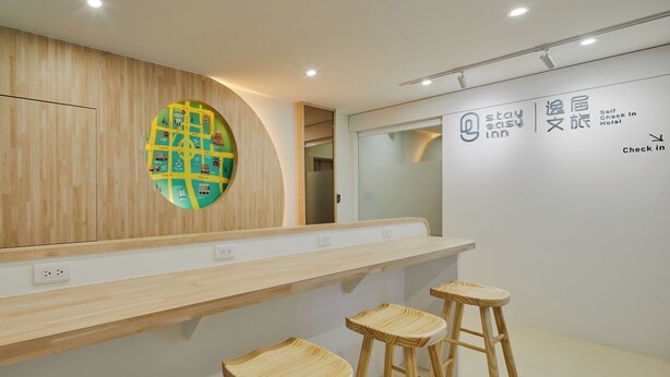 Un espace d’accueil moderne, avec un comptoir en bois, trois tabourets en bois et un panneau circulaire fixé au mur, orné de divers pictogrammes.