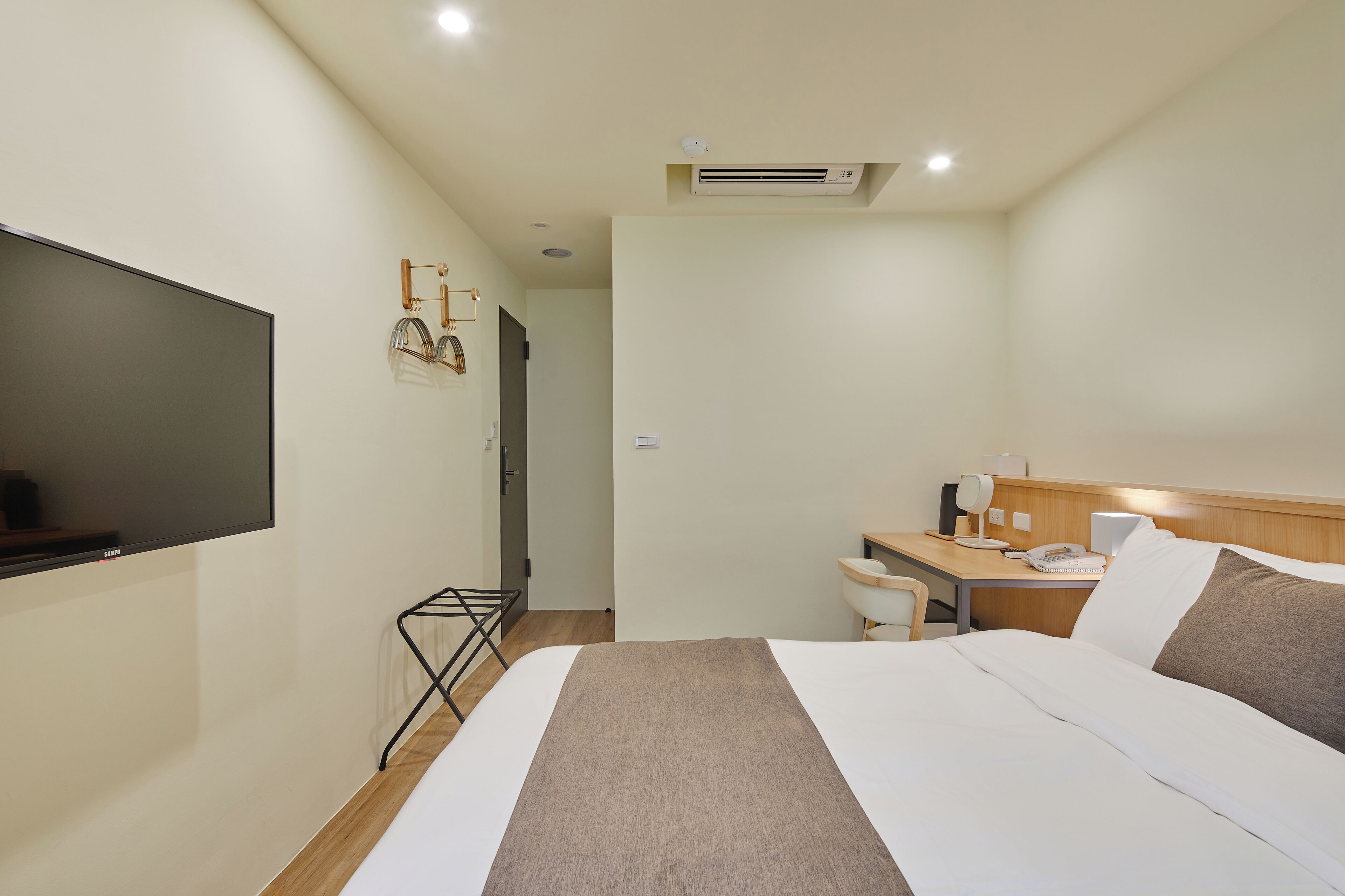 Ein Hotelzimmer mit einem Bett, einem Schreibtisch mit Stuhl, einem Flachbildfernseher und einer Klimaanlage.