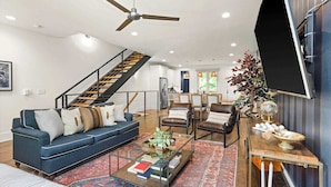 Un salon spacieux avec un canapé bleu, des fauteuils en cuir, une table basse et un escalier menant à un niveau supérieur.