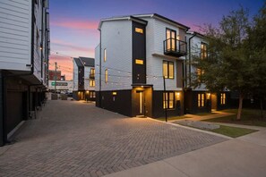 A modern residential building with a brick-paved driveway and a small front yard.