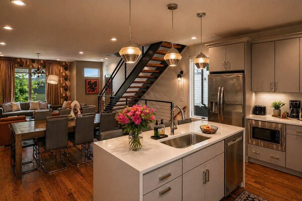 A modern kitchen with a central island, stainless steel appliances, and a dining area with a sofa and chairs.