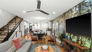 Ein modernes Wohnzimmer mit Treppe, Essbereich und großer Fernsehwand.