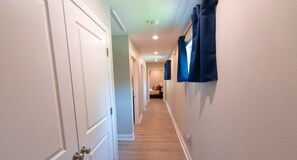 A hallway with white doors, a wooden floor, and blue curtains on the right wall.