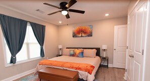 A bedroom with a bed, a ceiling fan, a painting, a bench, and a door.