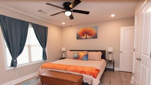 A bedroom with a bed, a ceiling fan, a painting, a bench, and a door. - Stylish 3BR Stay w/ Fast Wi-Fi + Parking (Jacksonville)