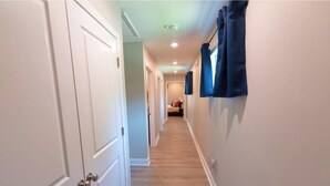 A hallway with white doors, a wooden floor, and blue curtains on the right wall. - Stylish 3BR Stay w/ Fast Wi-Fi + Parking (Jacksonville)