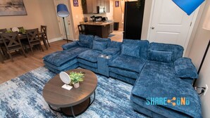 A modern living room with a sectional sofa, a round coffee table, and a dining area with a table and chairs. - Stylish 3BR Stay w/ Fast Wi-Fi + Parking (Jacksonville)