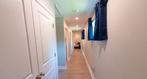 Un pasillo con puertas blancas, suelo de madera y cortinas azules en la pared derecha.