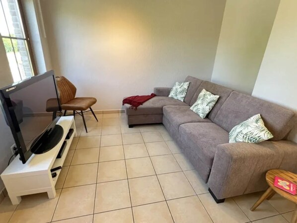 Ein Wohnzimmer mit Flachbildfernseher, braunem Ledersessel, grauem Sofa mit gemusterten Kissen und einem kleinen Holztisch.