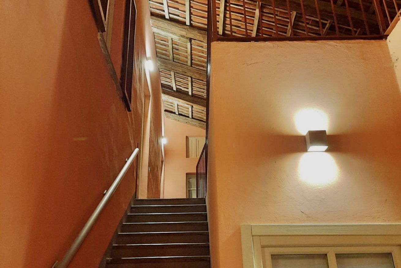 Eine Treppe mit Geländer, einer Wandleuchte und einer Holzdeckenkonstruktion.